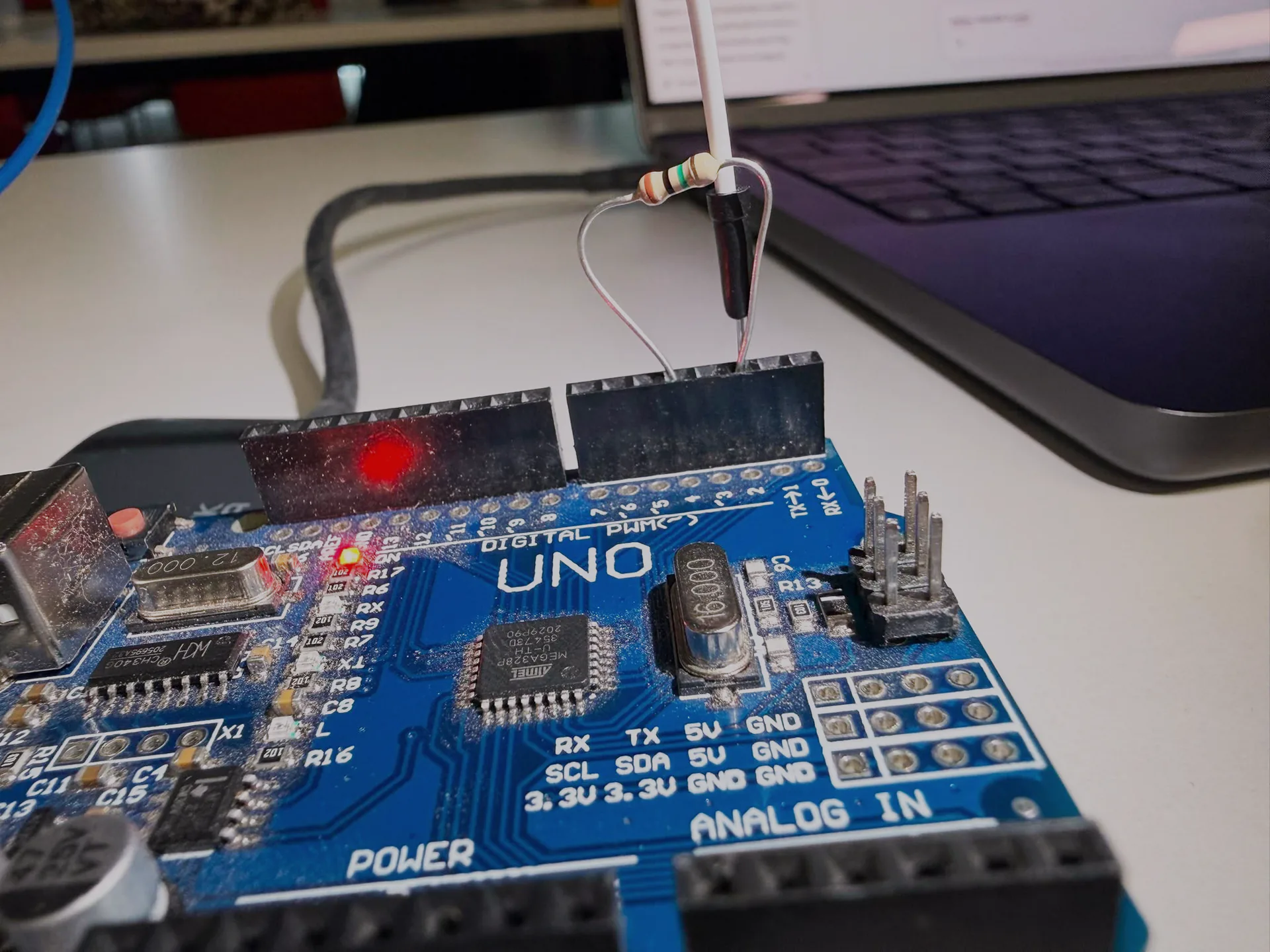 Close-up of an Arduino UNO with the resistor and the sensor wire seated in the header pins, its red LED lit.